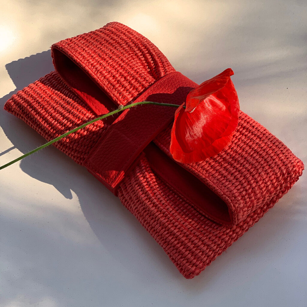 novinska red handbag, a fresh poppy flower laying on it and a tiny snail climbing a flower